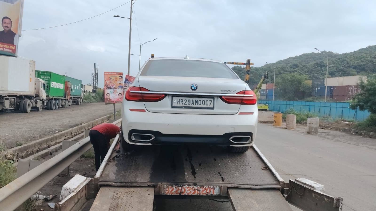 Siddhivinayak Towing safely loading a white BMW 7-Series luxury car onto a flatbed truck near the highway in Thane, Mumbai.